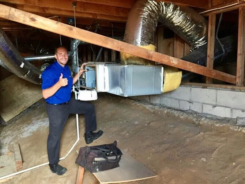 Steve Moore giving a thumbs up beside a new air handler and ductwork in a crawlspace
